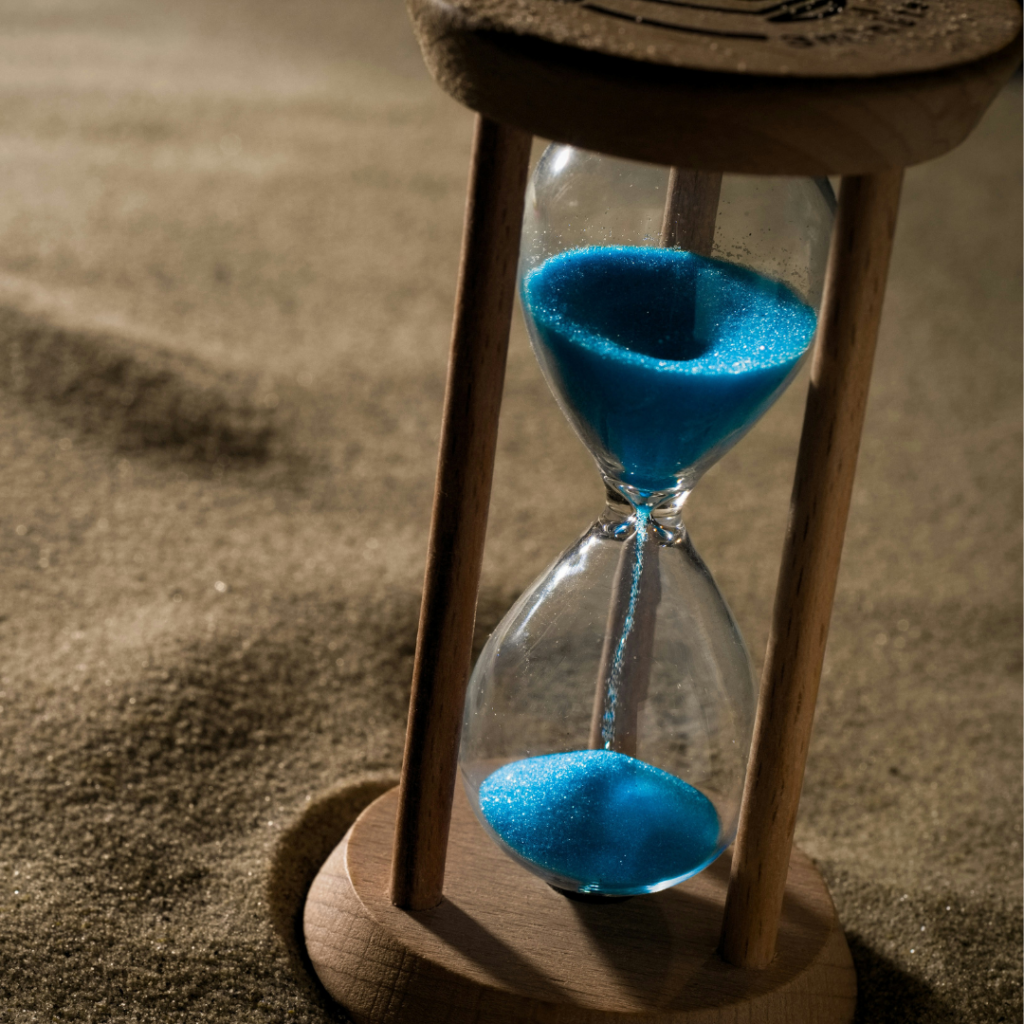 Hourglass with blue sand on a beach.