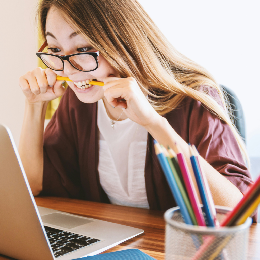 Woman biting a pencil while staring at her laptop.