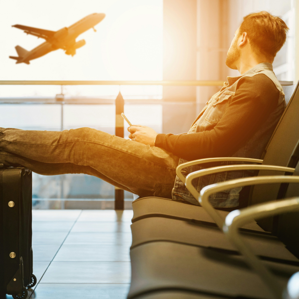Man resting his feet on his suitcase as he watches a plane take off in the background.