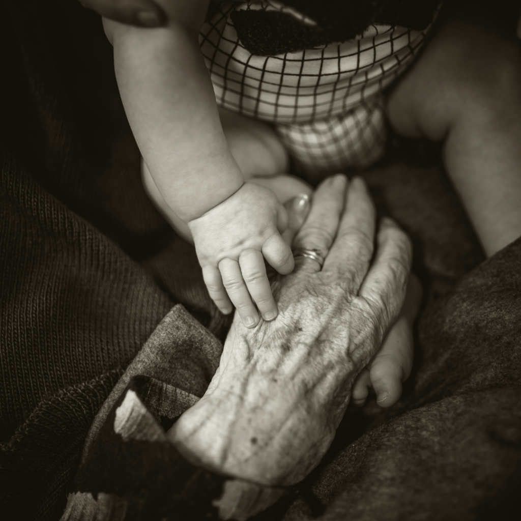 The change in years. A baby's hand on top of an elderly's hand in black and white. 
