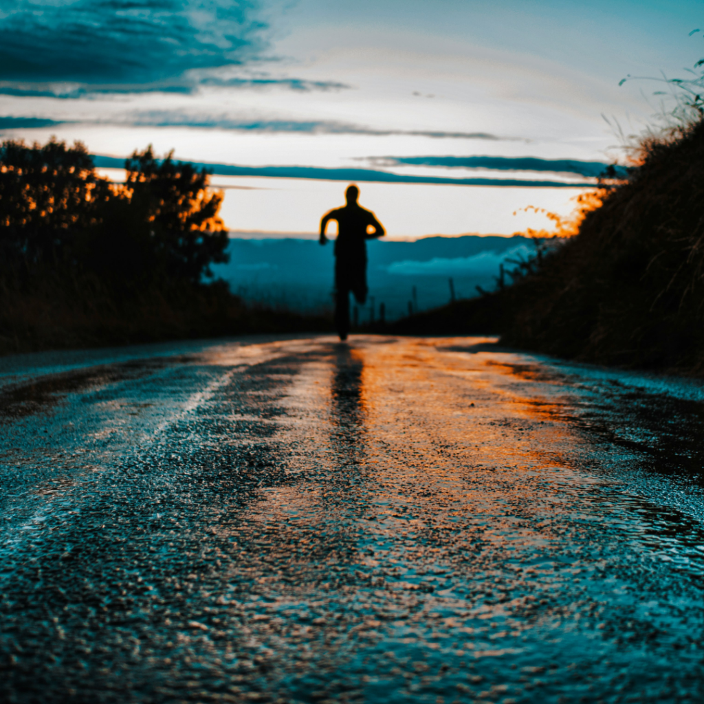 Figure running on a wet road, with threes on both sides,in the sunset.