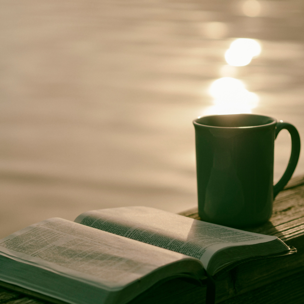 Calming picture of a cup of coffee and a book on the waterside.