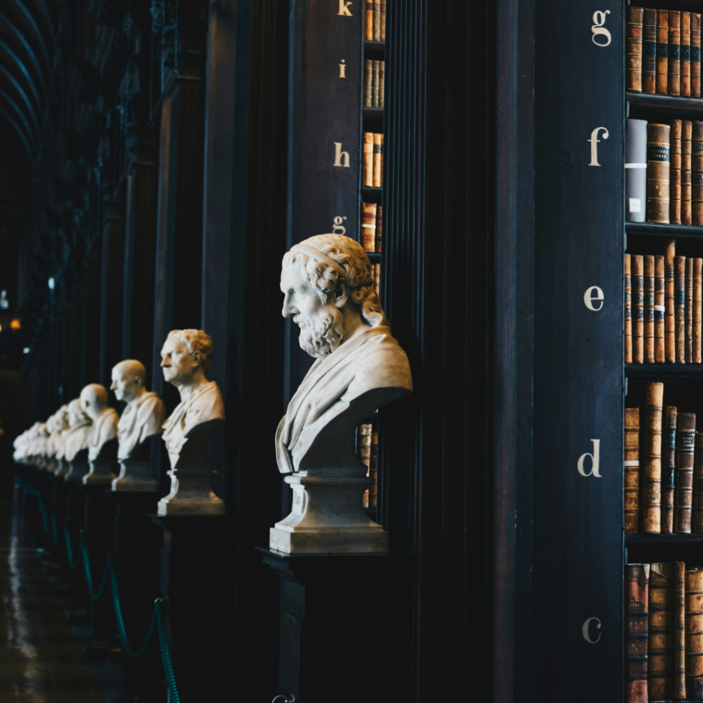 Picture of a library with statues in front of the rows.