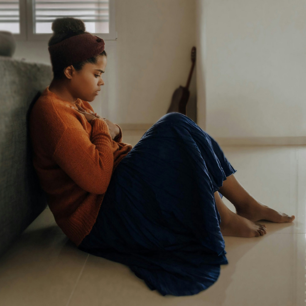 Woman sitting on the side of a bed with anxiety after receiving criticism.
