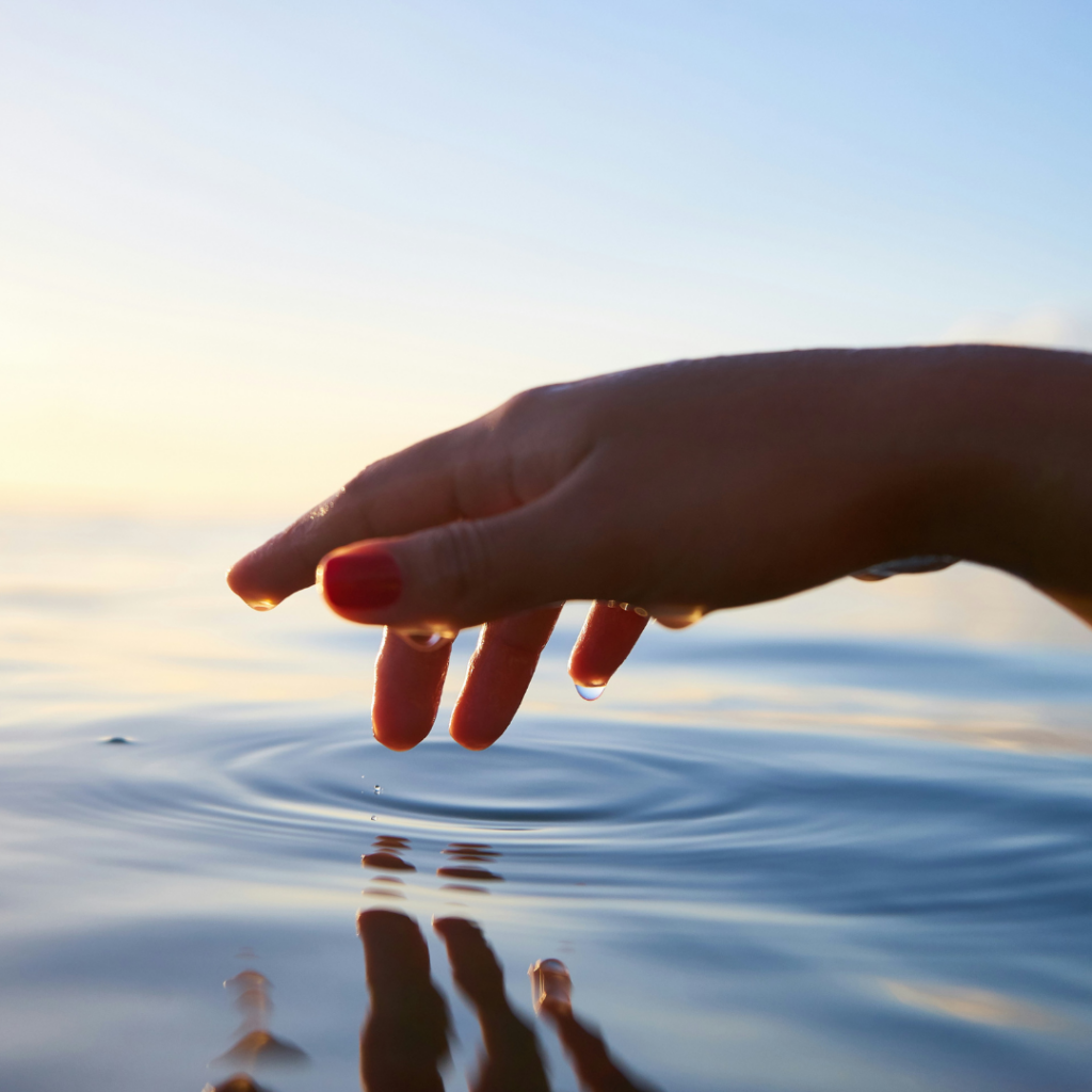 Mirror reflection in the water, as a hand touches the surface of some water.