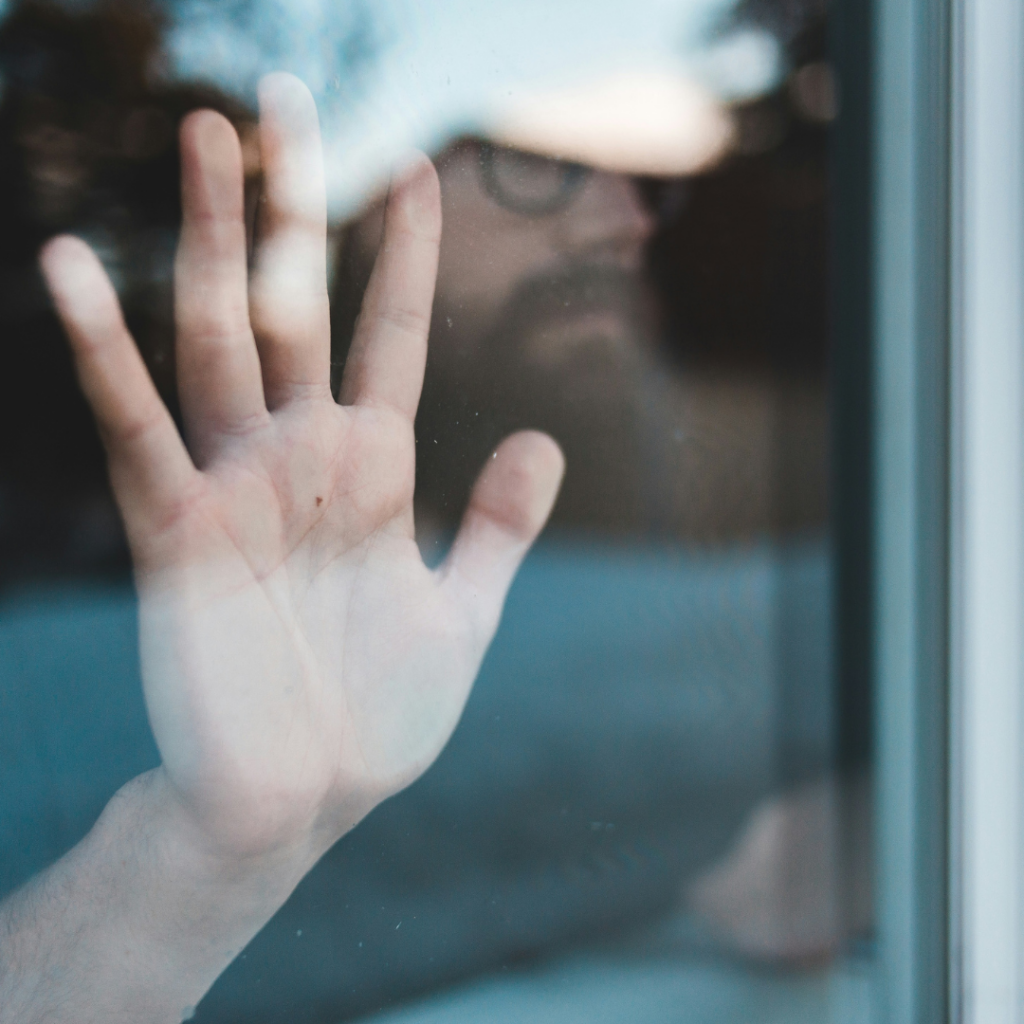Man with his hands against the window looking out while in lockdown.