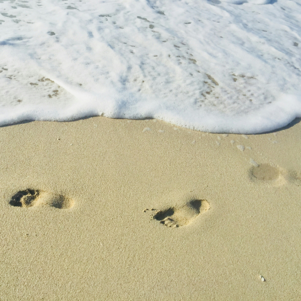 Foorprints on a beach with the sea creeping up on them.