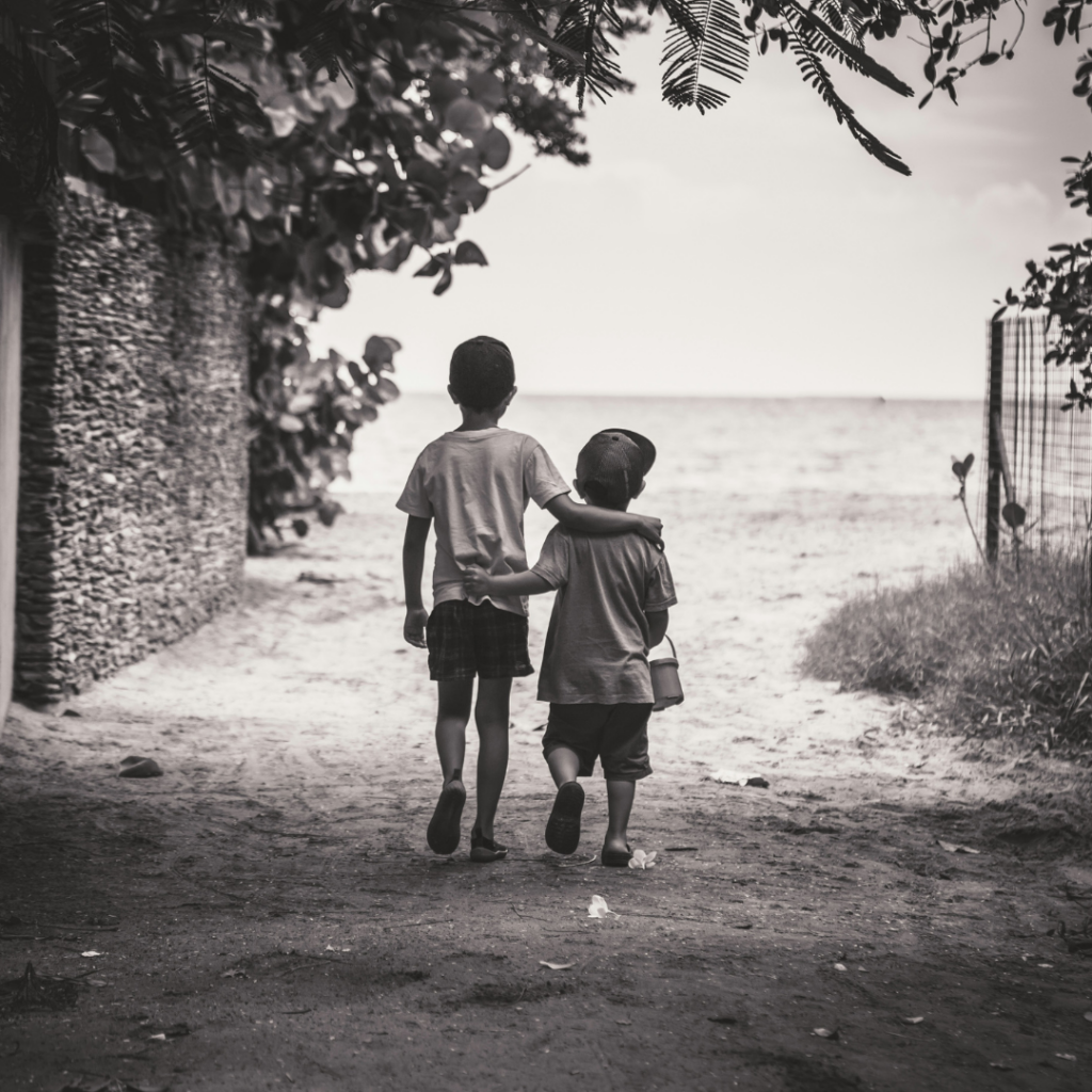 Two children walking with their arms over eachothers shoulders.