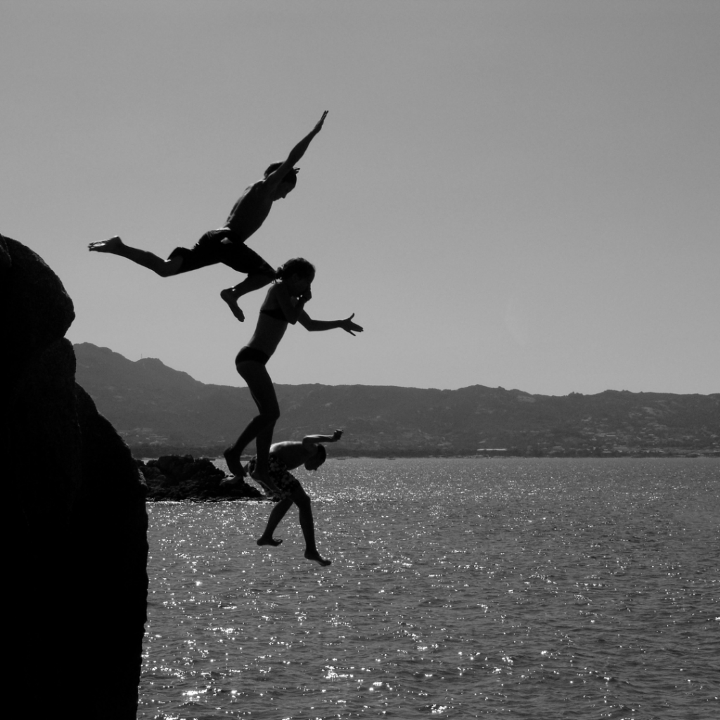 Three people jumping of a cliff in the water showing a lot of courage.