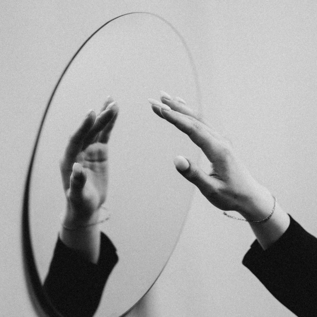 Hand almost touching a mirror.