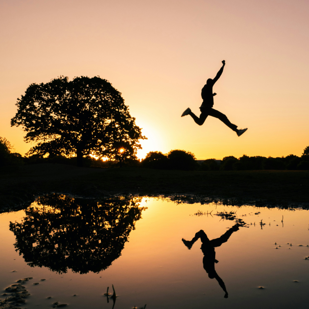 Man jumping over a lake at sunset.